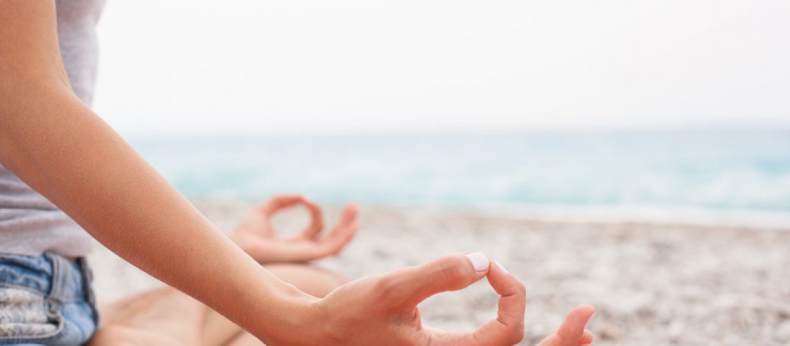 Young woman relaxing by practicing yoga on the beach, close-up of hands, gyan mudra and lotus position